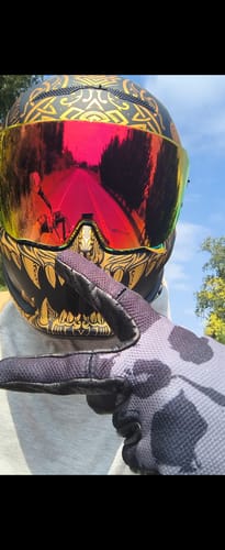 Customer's hand wearing a gray, patterned OG MX Glove, pointing toward a colorful motorcycle helmet.