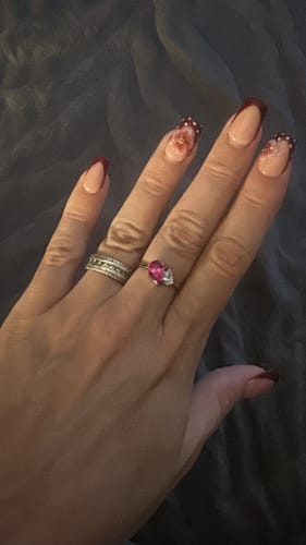 Customer's Leesha Birthstone Ring with a pink pear-cut stone on a polished metal band worn on a hand.