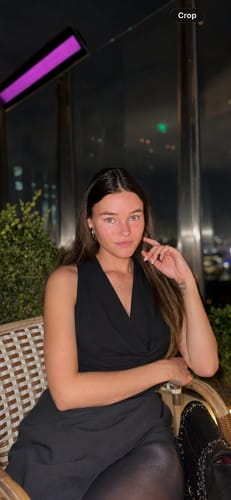 Customer's Celeste Cowl Neck Scarf Top, a sleek black sleeveless top worn in a dimly lit evening setting.