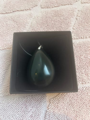Customer's Pendentif Obsidienne Oeil Céleste Goutte, a smooth dark stone pendant resting inside its open product box.