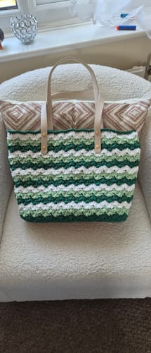 Customer's green and white wavy-striped crochet tote bag resting on a white chair.