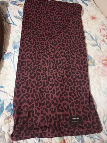 Customer's Buff Estampado Active tubular scarf with a dark purple and black leopard print pattern laid on a patterned bed.