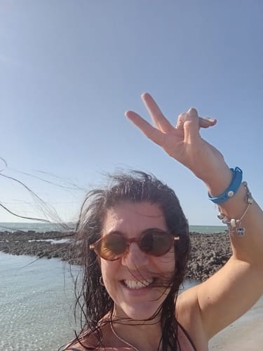 Customer's Positano sunglasses, round-framed, being worn by a person on a sunny beach.
