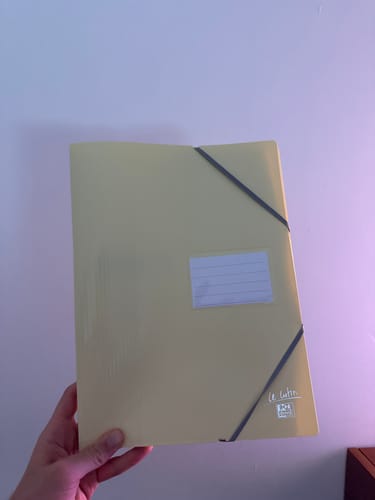 Avis d'un client tenant le porte-vues Oxford jaune pastel avec sa fermeture élastique et son étiquette d'identification.