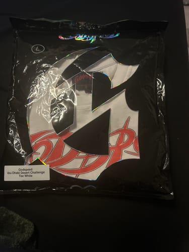 Customer's Godspeed Abu Dhabi Desert Challenge Tee White inside the sealed plastic packaging.