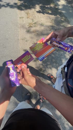 Customer's hands holding purple THC-A Cali Blend pre-roll packaging and a small information card outside.