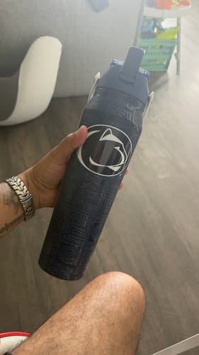 Customer's hand holding the dark blue Bottle Buddy with a Nittany Lions logo, seen indoors.