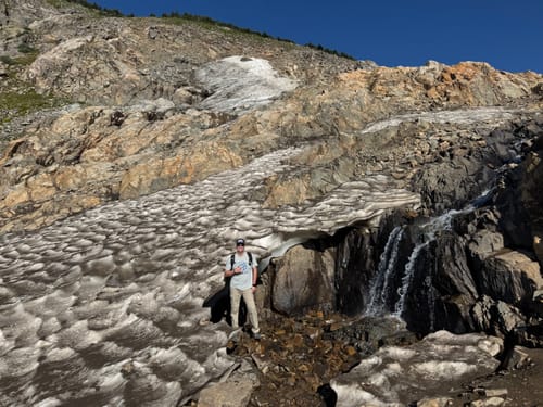 Customer's Bad Knees T-shirt worn while hiking in a rocky, snowy mountain landscape.