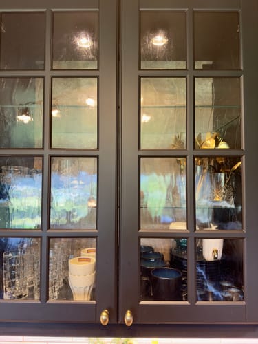 Customer's Rusty Gold kontaktplast visible as a textured backing through the glass-paneled doors of a black kitchen cabinet.