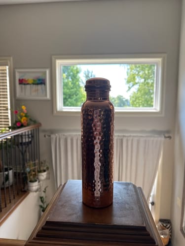 Customer's hammered copper water bottle standing on a wooden surface in a bright room.