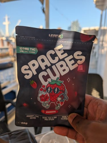Customer's hand holding a dark-colored LEAFZ Space Cubes strawberry gummy package.