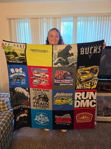 Customer's Project Repat T-Shirt Quilt held up by a person, showing a colorful 12-square layout of vintage graphic tees.