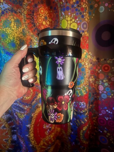 Customer's black To-Go Buddy Poisoned Petals tumbler held in hand with a vibrant, colorful patterned backdrop.