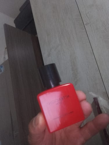 Customer's hand holding a bright red Attracione Men perfume bottle with a black cap.