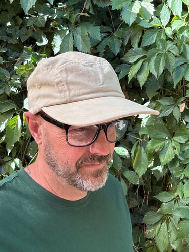 Customer's beige Big Camp Hat worn by a person, seen from a side angle against green foliage.