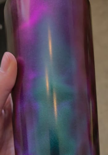 Customer's hand holding the Northern Lights Bottle Buddy, showing the vibrant purple and green iridescent finish.