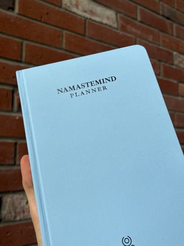Customer's light blue Namastemind planner being held in hand against a brick wall.