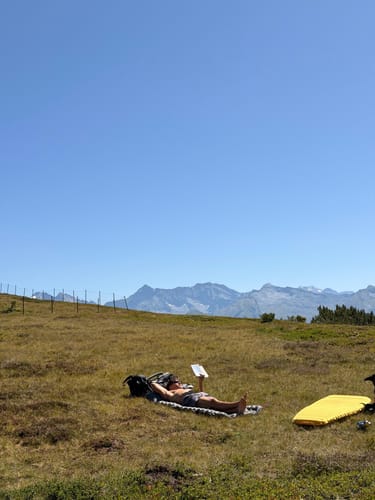 Customer's Isomatte used by a person reading a book while lying on the ultraleichte Isomatte in a sunny mountain landscape.