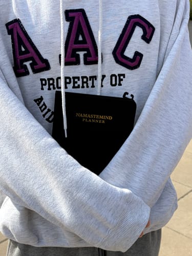 Reviewer's black NamasteMind Planner held in person's arms, wearing a light-colored sweatshirt.
