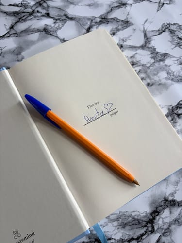 Customer's open Planner with a blue and orange pen resting on the page featuring a personalized handwritten signature.