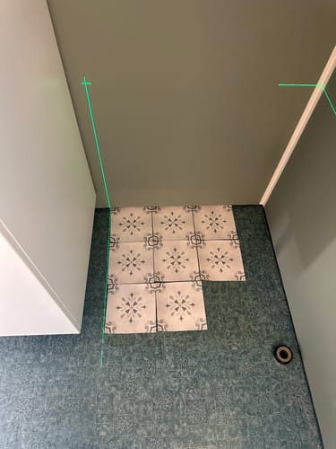 Customer's Amilia grønn selvklebende fliser partially installed on a bathroom floor using a laser guide.
