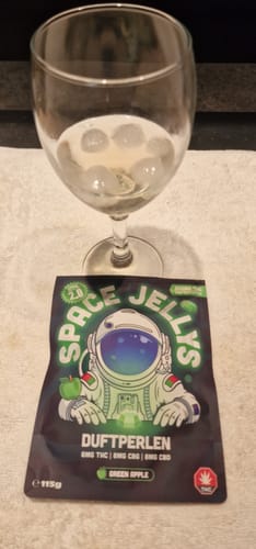 Kundenfoto der THC Spacejellies 2.0 Verpackung vor einem Weinglas mit Eiswürfeln auf einer weißen Unterlage.