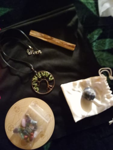 Reviewer's AuraBloom subscription box contents featuring a tree of life necklace, crystals, and a Palo Santo stick.