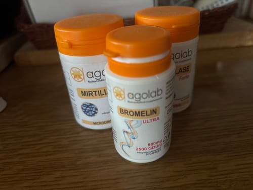 Reviewer's three bottles of Agolab supplements including Bromelin Ultra and Mirtillase on a wooden surface.