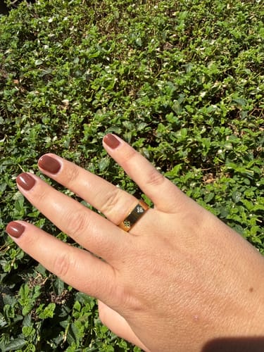 Customer's Eloise Birthstone Ring on a hand, featuring gold-plated band with delicate stone settings against green foliage.