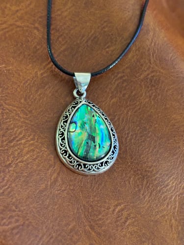 Customer's teardrop-shaped Abalone Shell necklace on a black cord against a brown background.