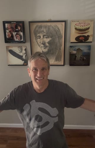 Customer's Record Adapter T-Shirt, a grey shirt with a graphic, worn by a smiling person in front of record art.