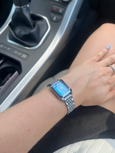 Customer's Claire De Mains watch with a blue dial and silver link band on their wrist while inside a car.