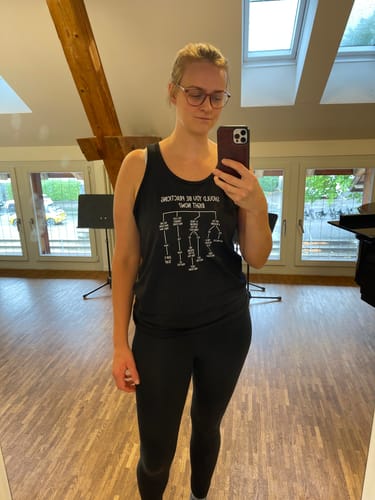 Customer's black Practicing Right Now Tank Top with white graphic print, worn by a person in a practice studio