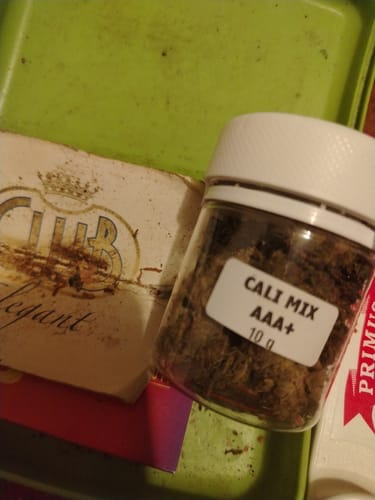 Customer's clear jar of CALI MIX AAA+ flower, sitting next to a branded card on a green surface.