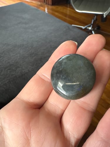 Customer's hand holding a smooth, round dark gray crystal from the VIP Crystal Club.