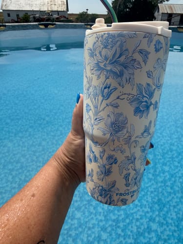 Customer's Blue Floral To-Go Buddy tumbler held in hand over a blue outdoor pool.