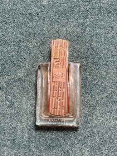 Customer's Protección perfume bottle with elegant rose-gold cap and label, shown against a textured gray background.