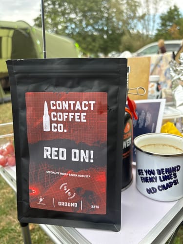 Customer's black bag of Red On! High-Caffeine Coffee standing on a table next to a cup with a humorous message.