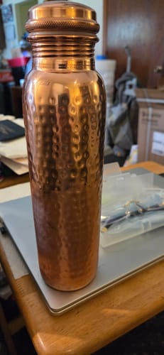 Customer's hand-hammered copper water bottle standing on a laptop surface.