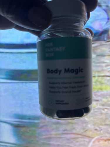 Customer's hand holding a bottle of Body Magic Chlorophyll pills, slightly blurry view.