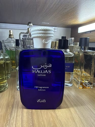 Customer's Perfume Hawas Sapphire bottle with deep blue glass, centered on a wooden shelf among other fragrance bottles.