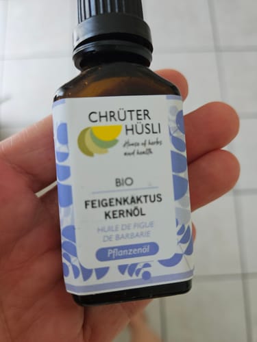 Kundenhand hält eine kleine, braune Flasche Kaktusfeigenkernöl Bio vor hellem Hintergrund.