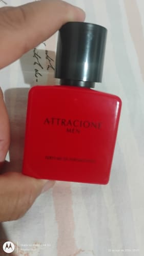 Reviewer's hand holding a square red Attracione Men perfume bottle with a black cap.