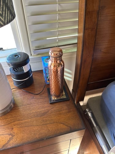 Customer's hand-hammered copper bottle resting on a wooden nightstand next to a lamp and small speaker.