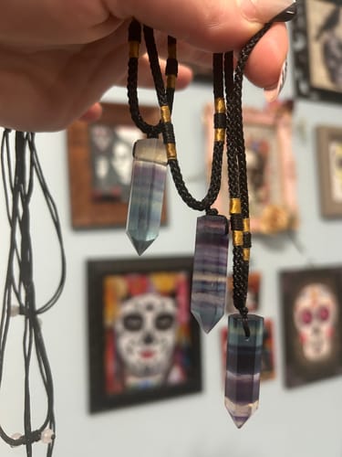Reviewer's hand holding three Natural Fluorite Necklaces with unique purple, blue, and green banded crystal pendants.