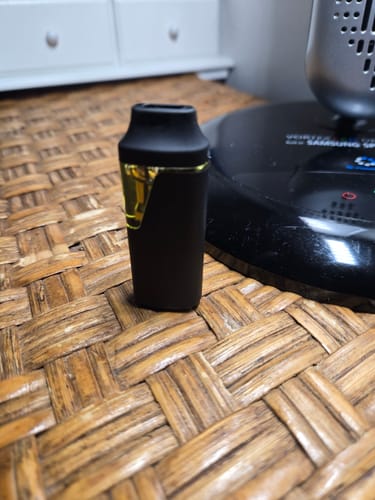 Customer's black PUR VYB OG Kush disposable vape device standing upright on a textured woven surface.