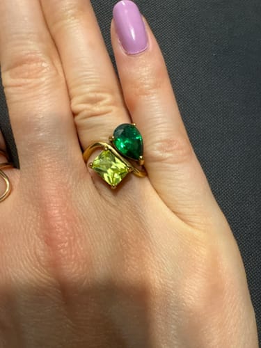 Reviewer's hand wearing the Navae Birthstone Ring, showing a gold-toned band with a pear-cut green and rectangle-cut light green stone.