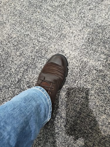 Customer's brown Sinister combat boot worn with blue jeans while standing on a gray speckled floor.
