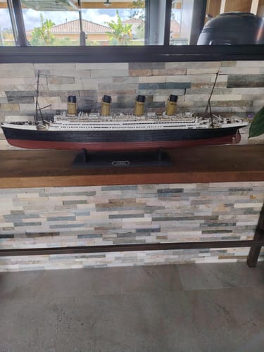 Customer's completed Maqueta Barco Titanic model sitting on a wooden surface in front of a stone wall.