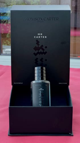 Customer's Mr Carter Eau de Parfum bottle placed inside its open black gift box on a pink surface.